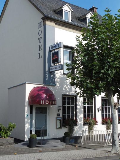 A cozy hotel building with a red awning and an inviting facade. In front of the hotel, there are some plants and trees.