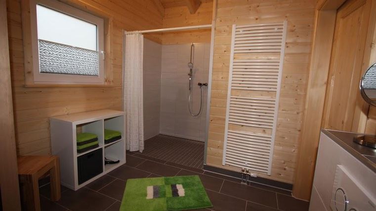 Ein modernes Badezimmer mit Holzverkleidung und einer Dusche. Es gibt ein Regal, einen Hocker und einen grünen Badeteppich.