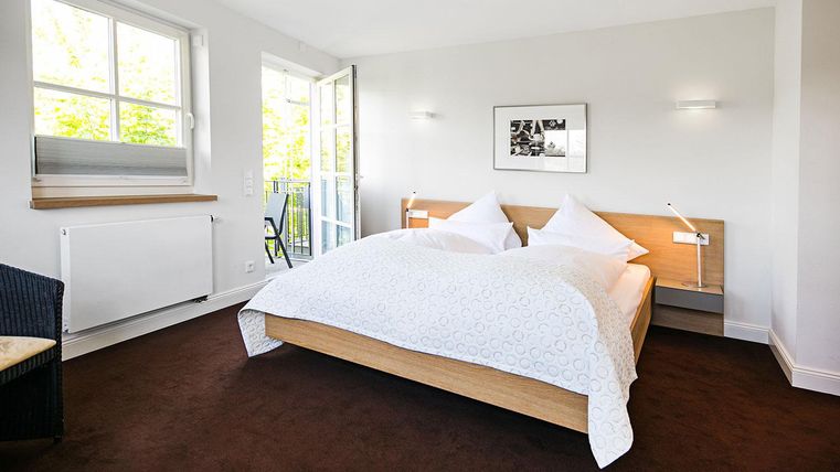 A bright and modern bedroom with a large double bed. The windows open onto a balcony and the room feels friendly and inviting.