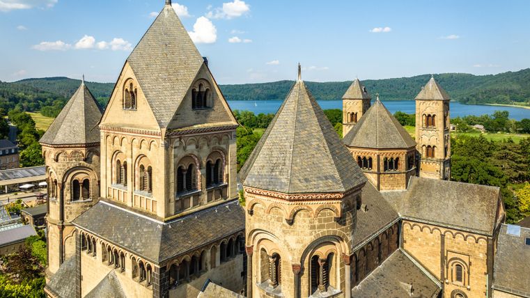 An impressive church with several towers and a picturesque view of the lake in the background. The sky is clear and the green hills complement the beautiful landscape.