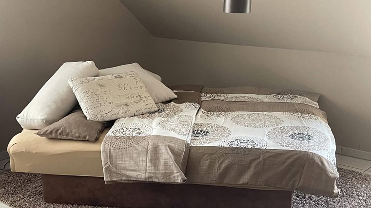 Ein gemütliches Bett mit Kissen und einer Decke in neutralen Farben. Der Raum hat eine warme Atmosphäre und ist einfach dekoriert.