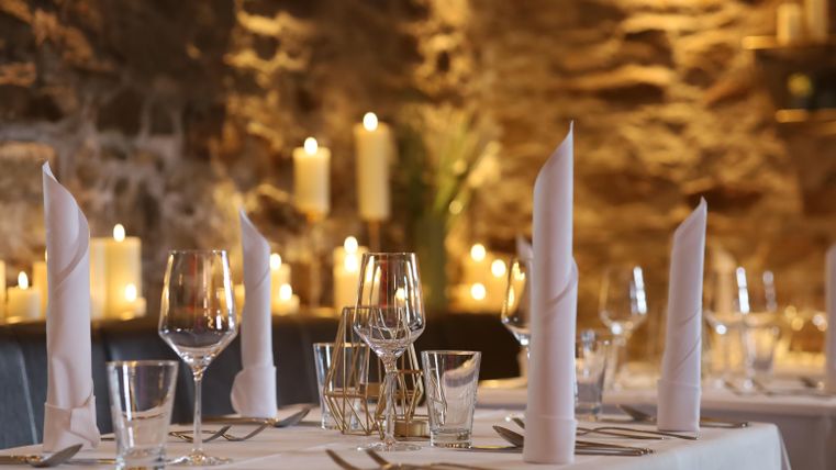 An elegantly set table in a cozy restaurant. In the background, candles glow and the stone wall creates a warm atmosphere.