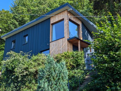 Ein modernes Haus mit einer Holz- und Metallfassade. Es ist von üppigem Grün umgeben und hat große Fenster.