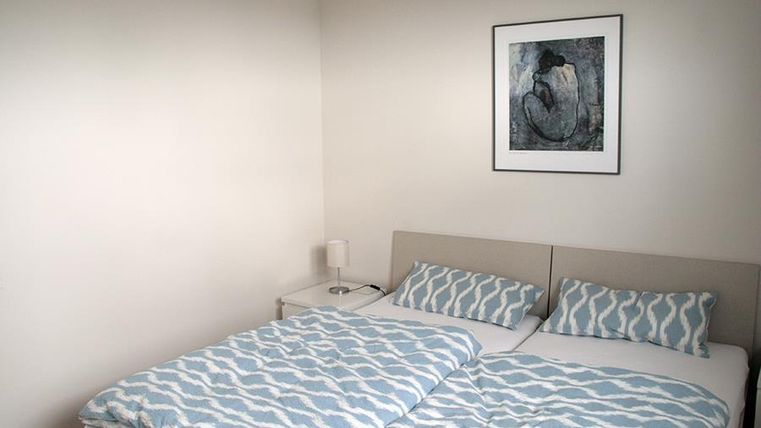 Ein gemütliches Schlafzimmer mit einem Doppelbett und blau-weiß gestreiften Bettdecken. An der Wand hängt ein Kunstwerk über dem Bett.