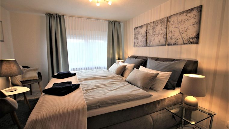Ein modernes Schlafzimmer mit einem großen Bett und eleganter Bettwäsche. Die Wände sind hell und die Fenster sind mit Vorhängen ausgestattet.