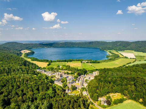 Ein schöner Blick auf einen See umgeben von Wäldern und Wiesen. Im Vordergrund sind kleine Gebäude und die Landschaft ist grün und sonnig.