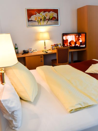 Ein gemütliches Hotelzimmer mit einem großen Bett 180x200cm. Ein Fernseher und ein Tisch mit Stühlen sind ebenfalls vorhanden.