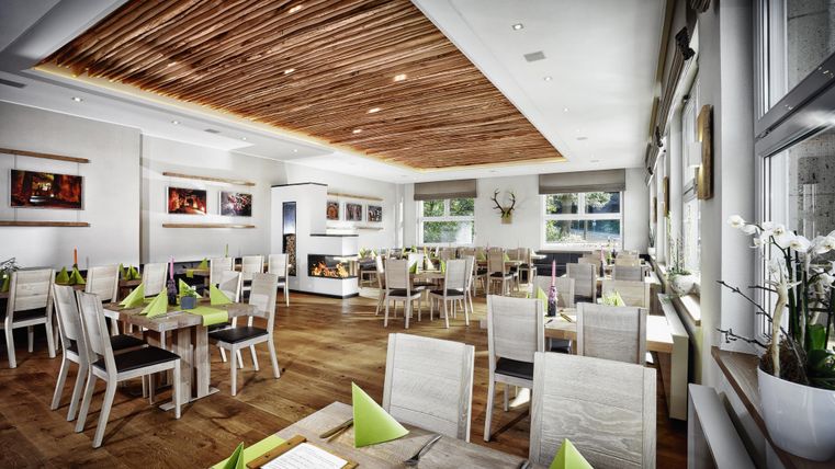 Ein modernes Restaurant mit Holzdecke und hellen Möbeln. Die Tische sind mit grünen Servietten dekoriert und es gibt große Fenster, die viel Licht hereinlassen.