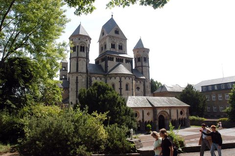 A historical church with several towers, surrounded by green spaces. In the foreground, some visitors can be seen exploring the area.