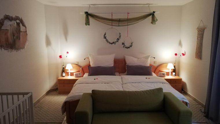 A cozy bedroom with two beds and soft lighting. A small seating area and a children's crib complement the tranquil atmosphere.