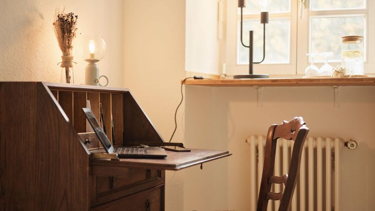 A cozy writing space with an old desk and a wooden chair. The window lets in soft light and creates an inviting atmosphere.