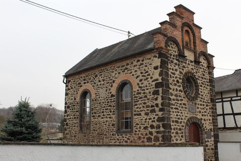 Ein historisches Gebäude aus Stein mit einem roten Ziegeldach. Es hat große Fenster und eine charakteristische Architektur.