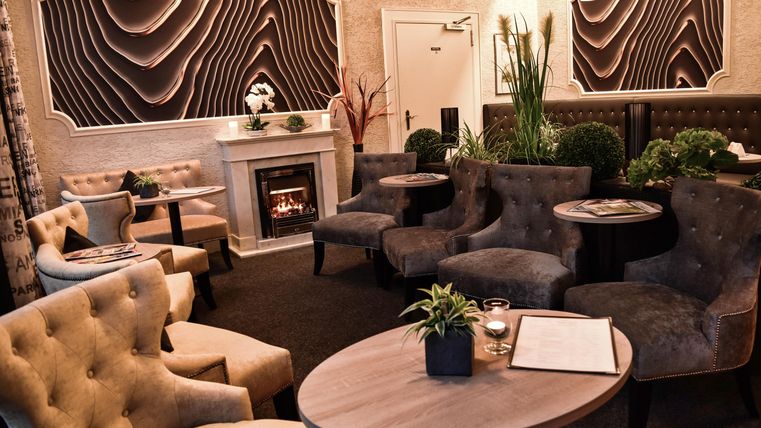 Elegante Lounge mit bequemen Sesseln und einem Kamin. Die Wände sind geschmackvoll dekoriert, und es gibt einige Pflanzen zur Verschönerung des Raumes. Einladende Atmosphäre zum gemütlichen Verweilen.
