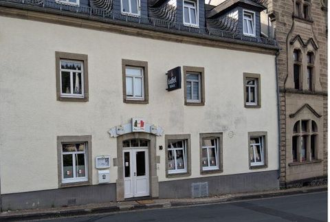 Een sfeervol, twee verdiepingen tellend gebouw met een lichte gevel. De voorkant toont meerdere ramen en een ingang die naar een winkel of een horecagelegenheid zou kunnen leiden.