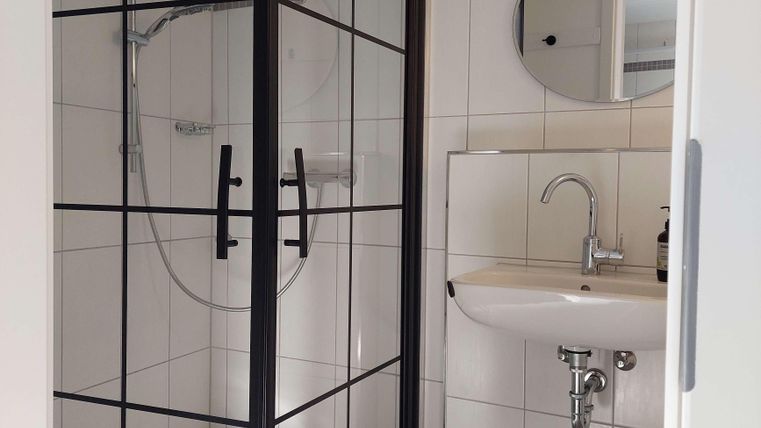 A modern bathroom with a glass shower stall and a sink. The walls are tiled and the space feels bright and inviting.