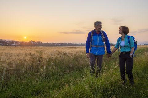 Ein Paar wandert bei Sonnenuntergang durch ein Feld, mit einer Stadt im Hintergrund.