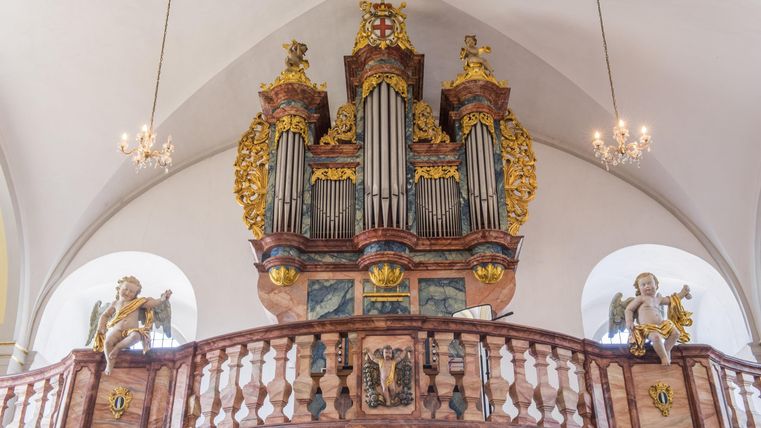 A magnificent organ with elaborate decorations in a church. Above the organ are golden details and two angel statues.