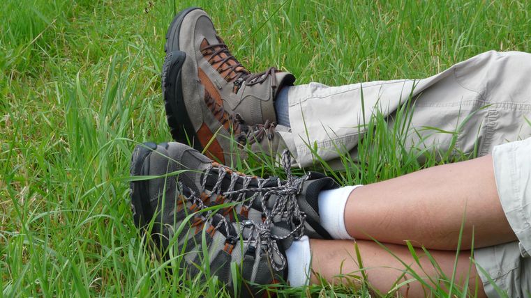 Two pairs of hiking boots are lying in the grass. The surroundings are green and natural.