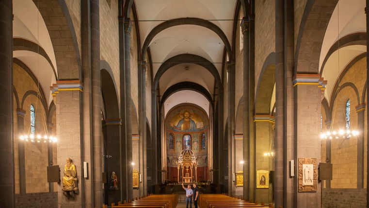 Ein schöner Kircheninnenraum mit hohen Gewölben und Holzbänken. Im Hintergrund ist ein Altar mit religiösen Bildern zu sehen.