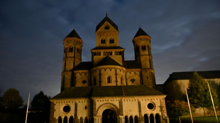 Eine beeindruckende Kirche mit mehreren Türmen, erleuchtet bei Nacht. Der Himmel ist bewölkt und vermittelt eine mystische Atmosphäre.