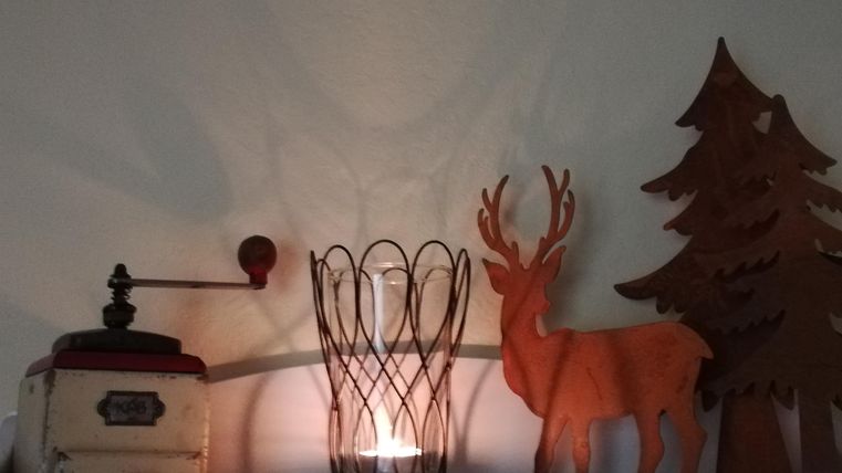 A cozy decoration with an old coffee grinder, a tealight in a basket, and a wooden deer next to a tree. The warm colors create an inviting atmosphere.