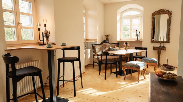 A bright and inviting dining room with wooden flooring and elegant furniture. Large windows provide plenty of daylight and a cozy atmosphere.