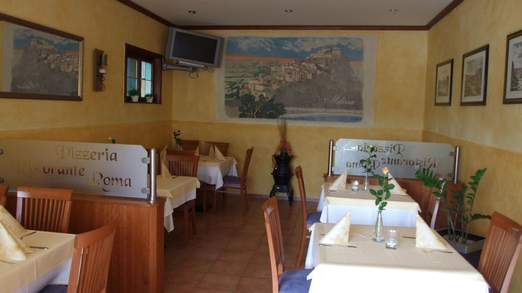 Ein gemütliches Restaurant mit Holztischen und gelben Wänden. An den Wänden hängen Bilder und es gibt stilvolle Tischdekorationen.