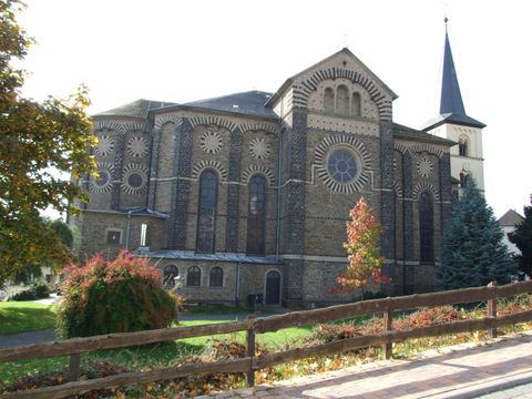 A historic church with a tall tower and beautiful windows. Surrounded by trees and colorful autumn leaves.