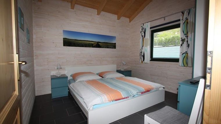 Ein gemütliches Schlafzimmer mit einem großen Bett und bunten Bettwäsche. Die Wände sind hell und die Fenster lassen viel Licht herein.