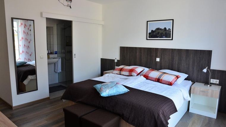 Ein modernes Schlafzimmer mit einem Doppelbett und bunten Kissen. Der Raum hat einen großen Spiegel und Zugang zu einem Badezimmer.