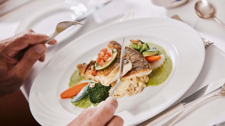 Ein köstlicher Teller mit gebratenem Fisch, Gemüse und Risotto. Die Speise wird von einer Hand mit Besteck gehalten.