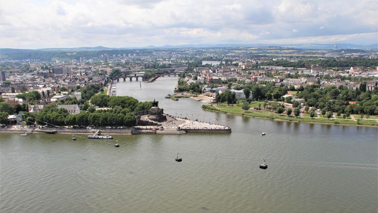 Eine malerische Stadtansicht mit einem Fluss und Brücken. Am Ufer sind grüne Bäume und einige Boote zu sehen.