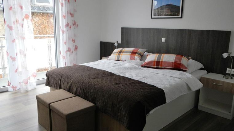 Ein modernes Schlafzimmer mit einem Doppelbett und bequemen Kissen. Die Fenster sind mit Vorhängen dekoriert und es gibt einen kleinen Tisch.