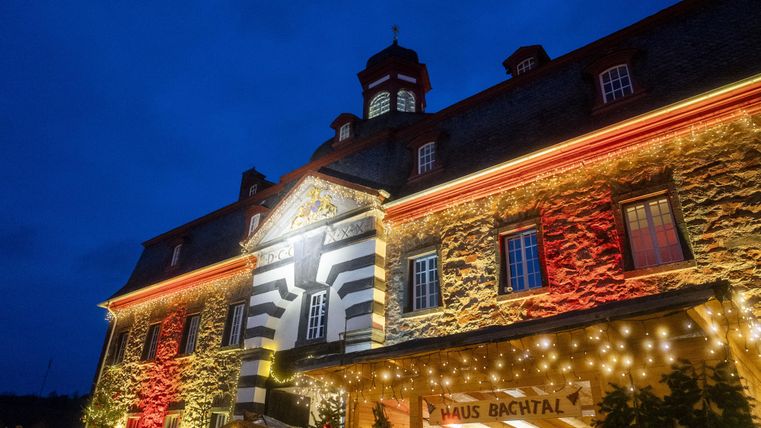 Ein historisches Gebäude mit bunten Lichtern bei Nacht. Der Himmel ist dunkelblau und die Atmosphäre ist festlich.