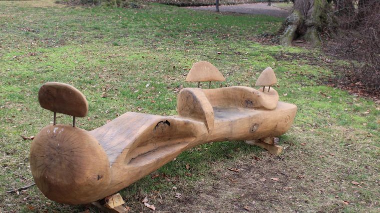 Eine kreative Holzbank, die wie ein Tier gestaltet ist. Sie steht in einem ruhigen Park auf grünem Gras.