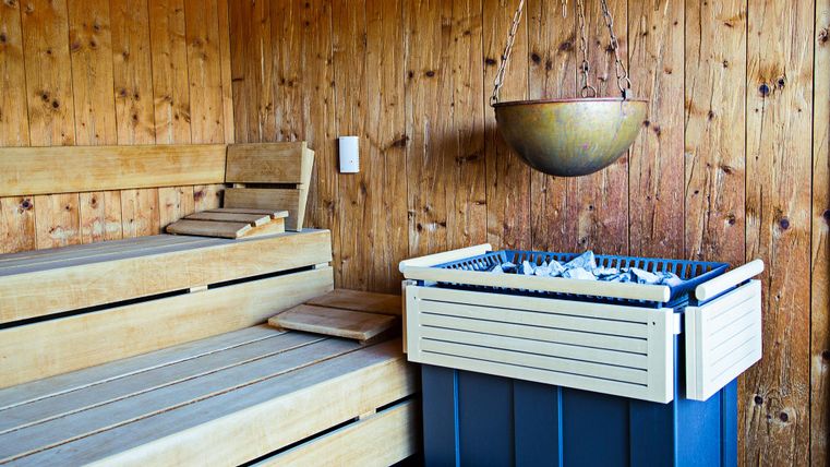 A cozy sauna with a wooden bench and a container for sauna infusions. The walls are made of wood, creating a relaxing atmosphere.