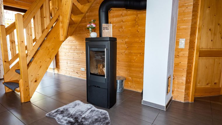 A modern wood stove stands in a wood-paneled room. The staircase and tiled floor create a cozy living area.