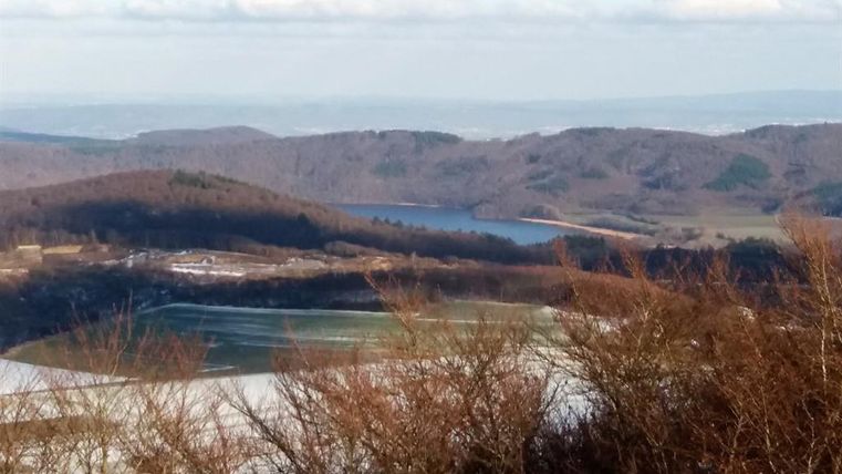 Eine malerische Landschaft mit sanften Hügeln und einem ruhigen Gewässer. Der Himmel ist bewölkt und die Natur ist im Winterlook.
