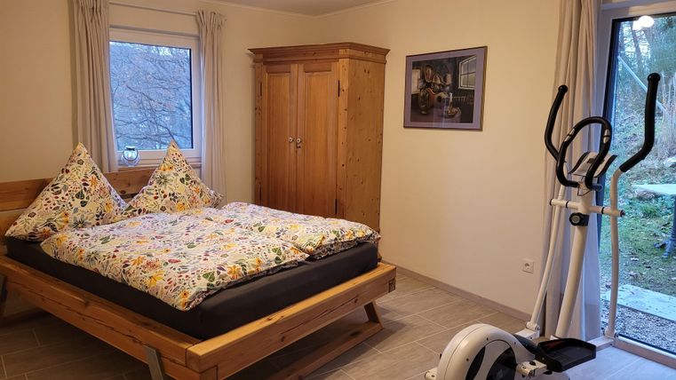 Ein helles Schlafzimmer mit einem großen Bett und gemütlichen Kissen. Im Raum steht auch ein Fitnessgerät und es gibt einen Zugang zum Außenbereich.