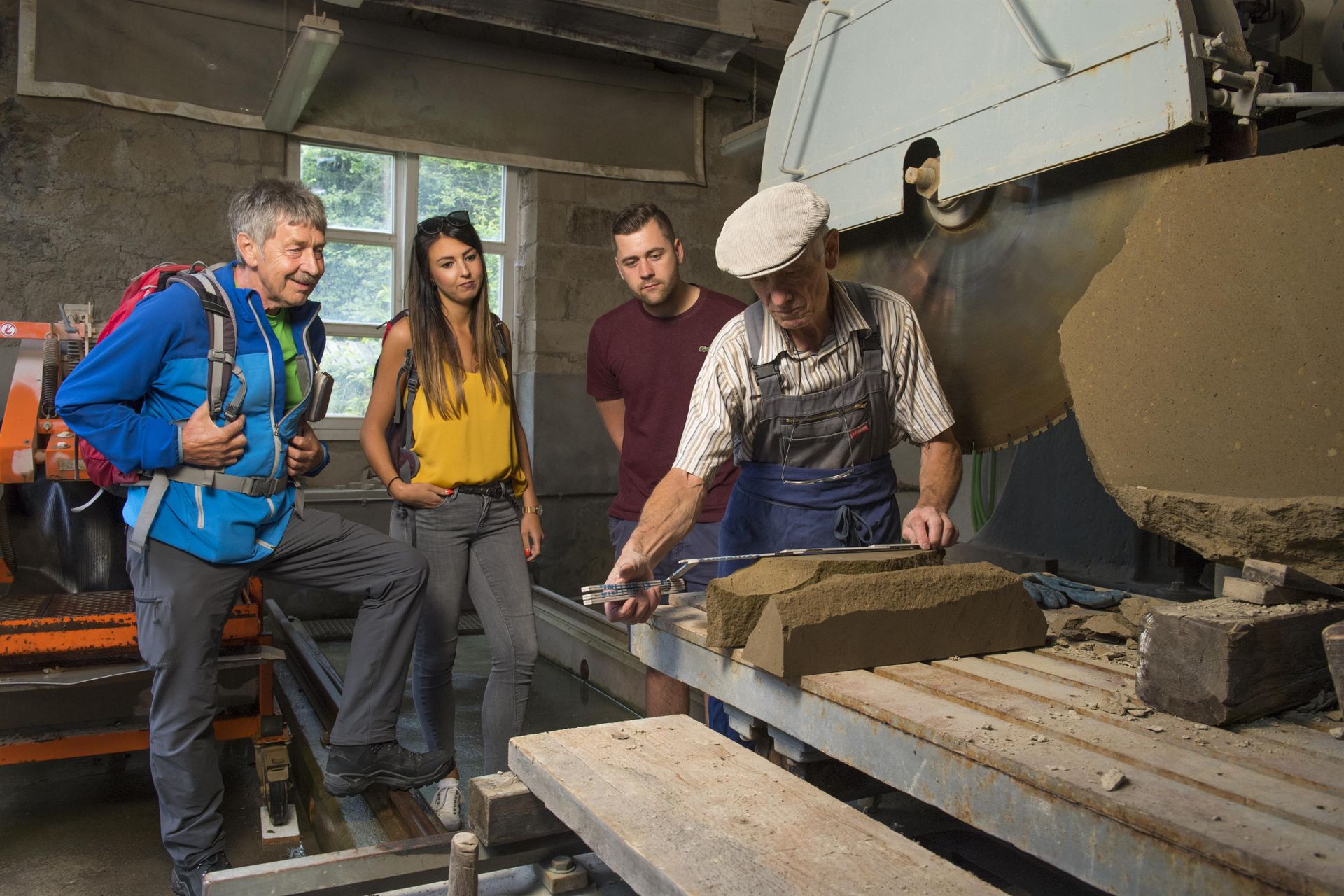 A group of four people is observing a craftsman working on a stone processing machine. The atmosphere is educational and artisanal.
