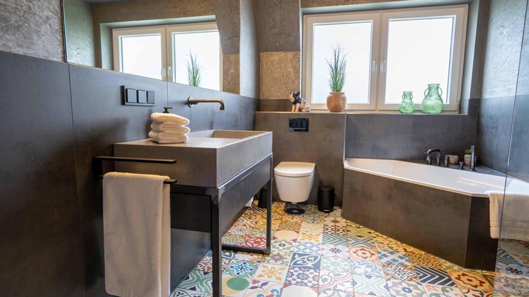 Ein modernes Badezimmer mit buntem Fliesenboden, einem stilvollen Waschbecken und großen Fenstern. Die Einrichtung ist minimalistisch und einladend, mit Pflanzen für einen frischen Akzent.