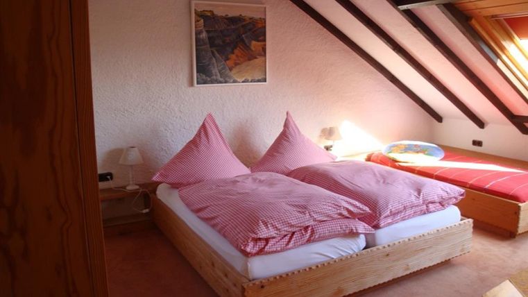 Ein gemütliches Schlafzimmer mit einem Doppelbett und einem Einzelbett. Die Wände sind hell, und das Zimmer hat eine schrägen Decke mit Holzverkleidung.