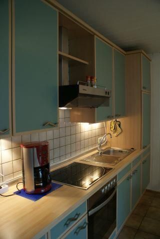 Eine moderne Küche mit blauen Schränken und Holzregalen. Auf der Arbeitsfläche sind eine Kaffeemaschine und Kochstellen zu sehen.