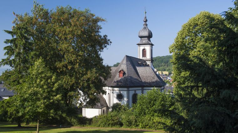 A picturesque church surrounded by trees and green grass. The sky is clear and blue.