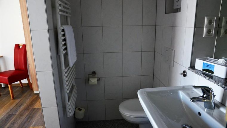 Ein modernes Badezimmer mit Fliesenwänden und klaren Linien. Im Vordergrund sind ein Waschbecken und eine Toilette zu sehen, während ein Handtuchhalter an der Wand hängt.