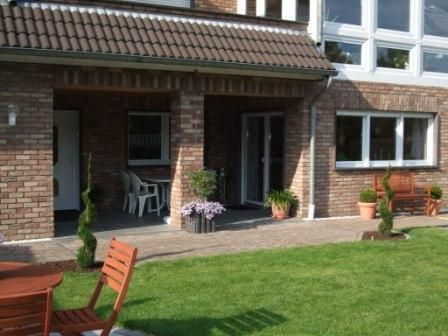 Ein gemütlicher Außenbereich mit einer Terrasse und Rasenflächen. Mehrere Pflanzen und Gartenmöbel verleihen dem Raum eine einladende Atmosphäre.