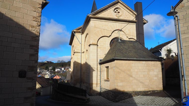 Eine alte Kirche aus Stein in einer engen Gasse. Der Himmel ist klar und blau, und die Umgebung wirkt ruhig.