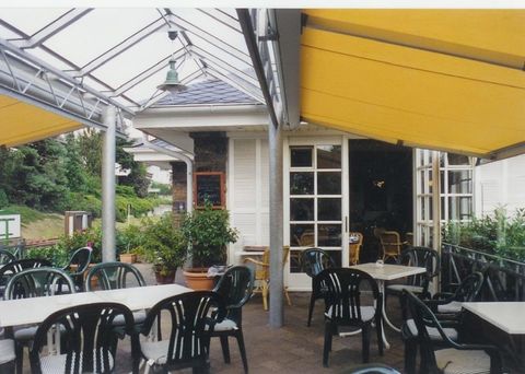Ein gemütlicher Außenbereich eines Restaurants mit schwarzen Stühlen und Tischen. Gelbe Markisen schützen vor der Sonne und umgeben von grünen Pflanzen.