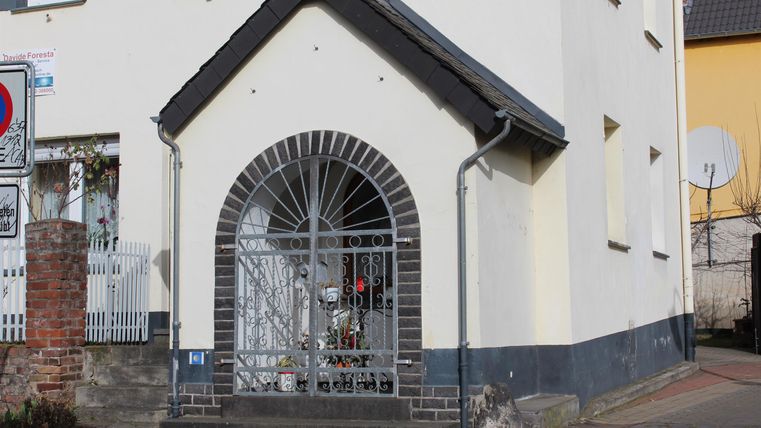 Ein dekorativer Eingangsbereich mit einem geschwungenen Tor. Die Fassade ist hell gestrichen und zeigt architektonische Details.