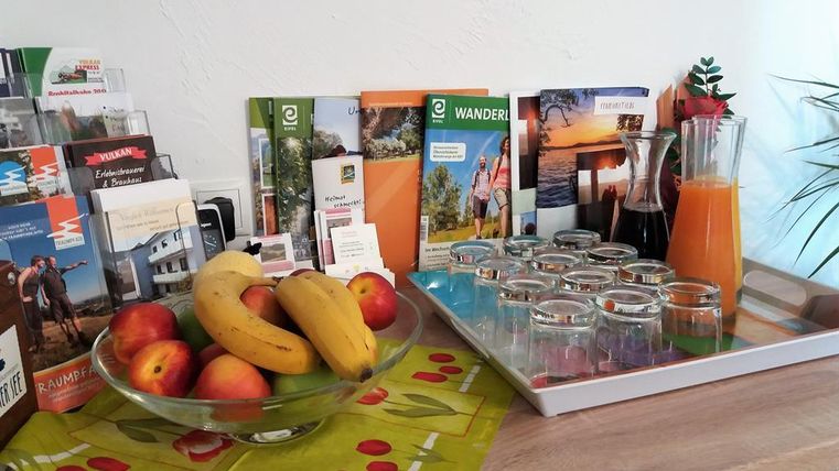 Ein Tisch mit einer Obstschale und Informationsbroschüren für Wanderungen. Daneben steht ein Tablett mit Gläsern und einer Karaffe mit Orangensaft.